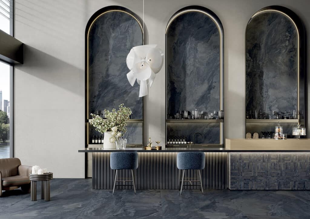 Bar moderne et luxueux avec trois arches murales en marbre noir rétroéclairées par des LED, un lustre blanc sculptural et des tabourets bleus.