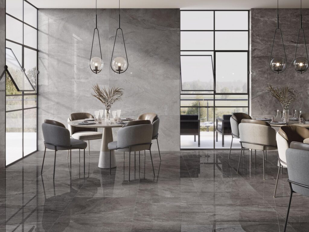 Salle à manger moderne avec carrelage gris foncé brillant, murs en pierre naturelle et grandes fenêtres à cadres noirs, éclairée par des suspensions design.