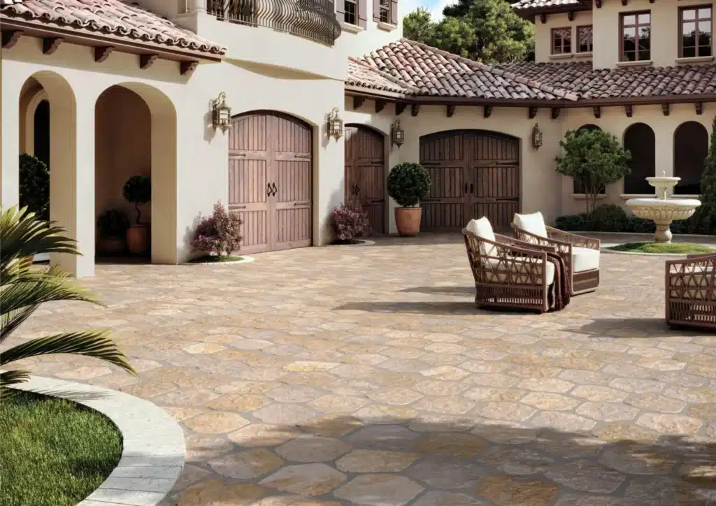 Grande cour pavée de dalles de pierre naturelle hexagonales couleur ocre devant une villa méditerranéenne avec portes en bois et fontaine.