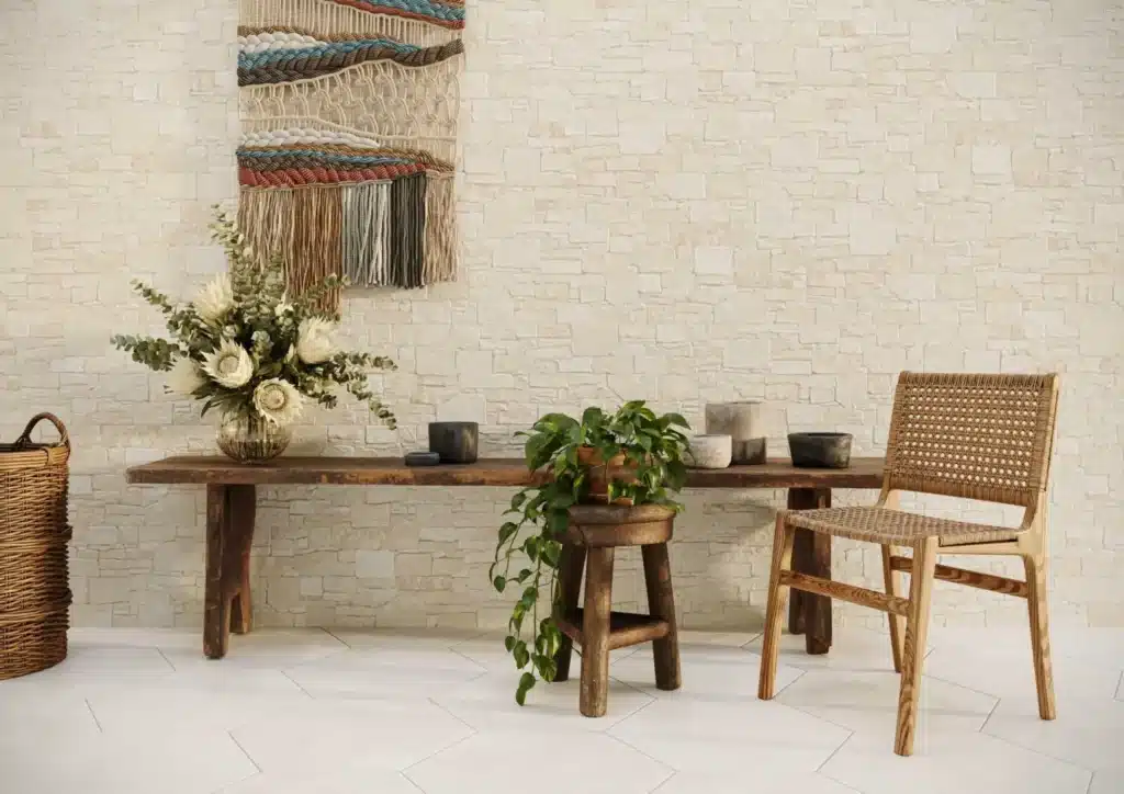 Ambiance bohème et naturelle avec mur en pierre claire, banc rustique, fauteuil en cannage et tissage mural coloré.