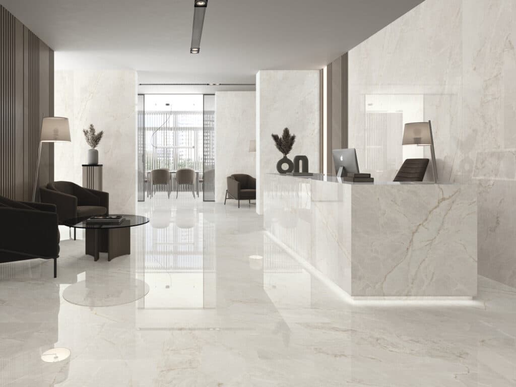 Lobby moderne avec sol et comptoir en marbre poli beige-crème veiné or, mobilier contemporain sombre, et bureau d'accueil.