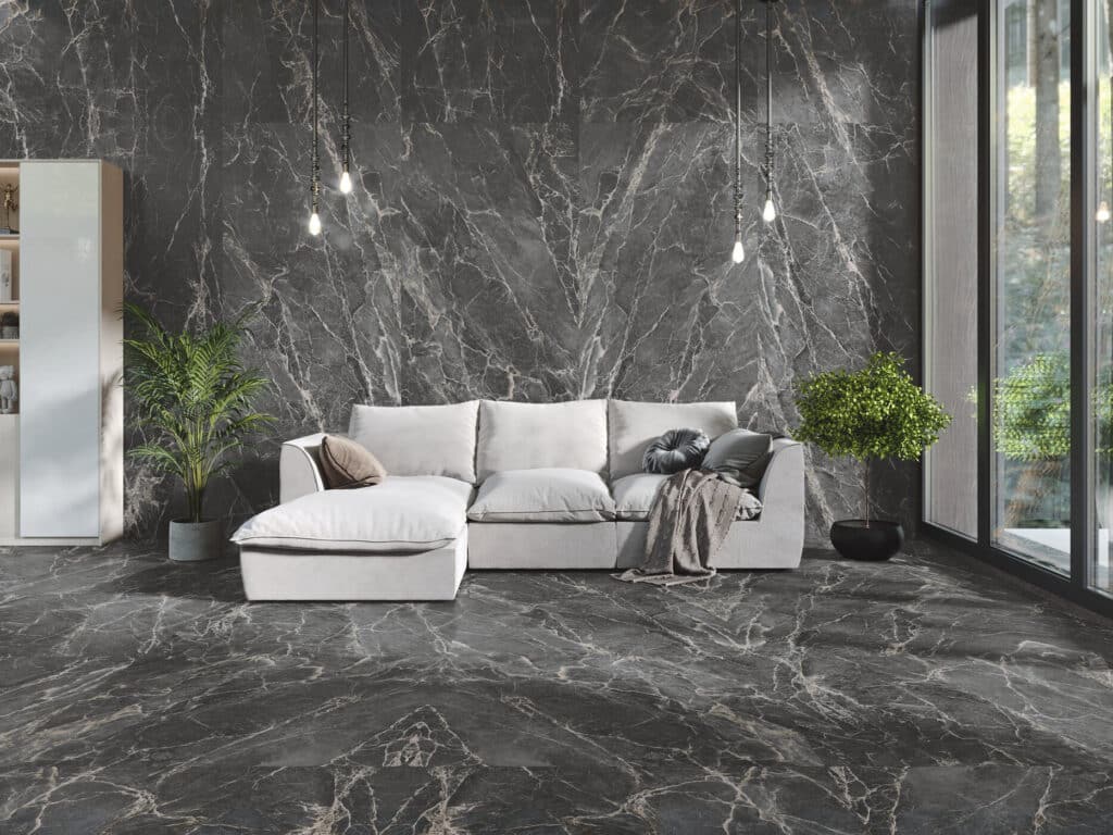 Salon moderne avec mur et sol en marbre noir veiné blanc, canapé sectionnel blanc, luminaires suspendus industriels et plantes vertes.