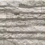 Texture de revêtement mural en pierre ou carreau de parement, grise et blanche, avec des bandes horizontales sculptées et rugueuses.