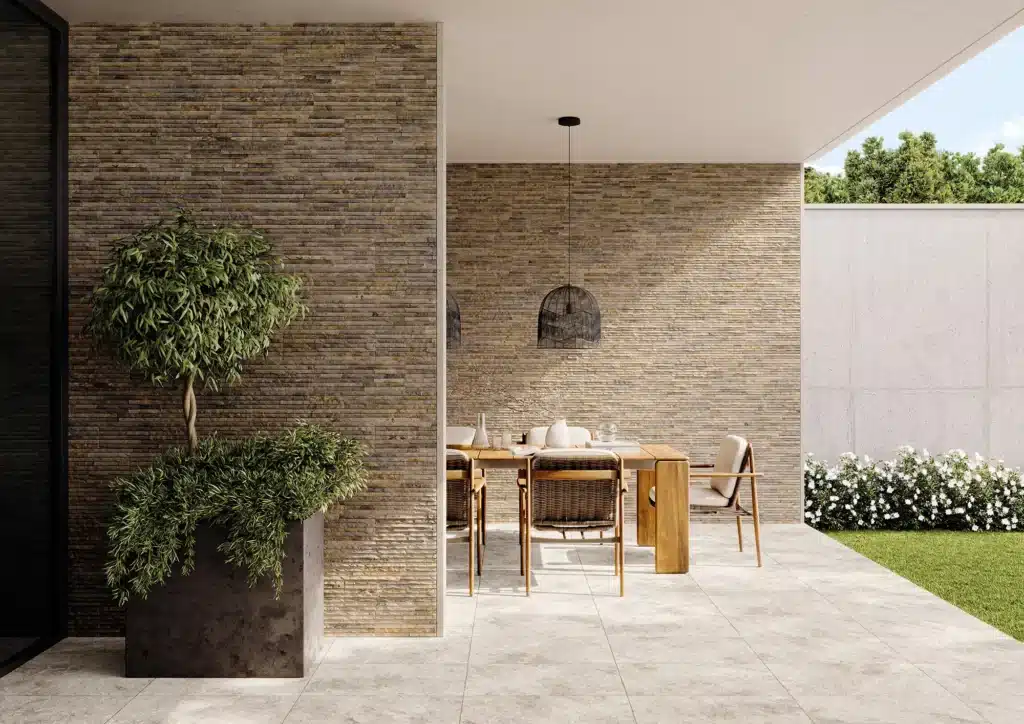 Patio extérieur moderne avec murs en pierre empilée texturée, mobilier en bois et rotin, suspension noire et verdure luxuriante.