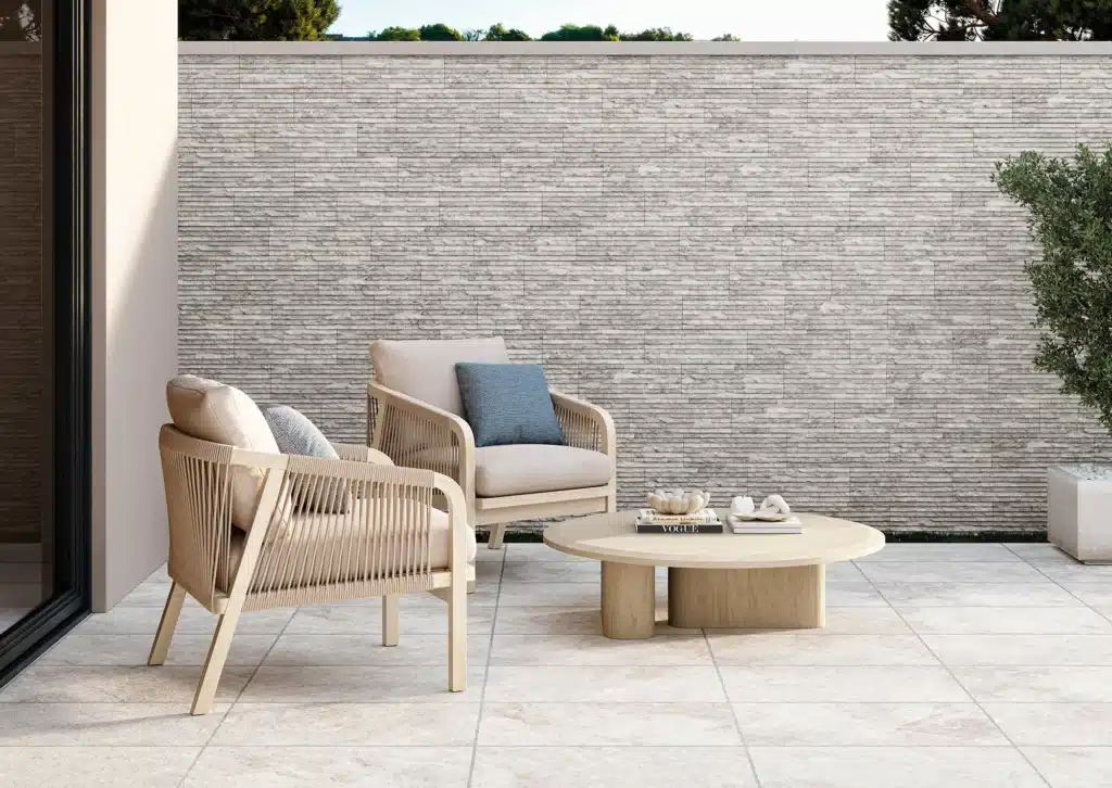 Patio extérieur moderne avec deux fauteuils en corde claire et table basse, mur en pierre naturelle claire et carrelage beige.