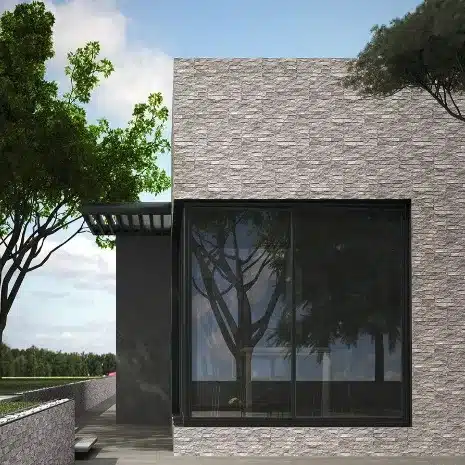 Façade moderne avec revêtement en pierre grise texturée et une grande baie vitrée foncée reflétant un arbre en pleine nature.