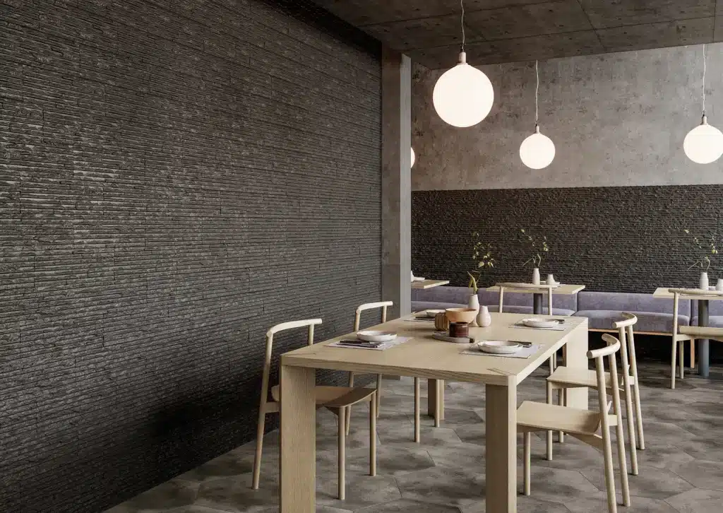 Intérieur de restaurant moderne avec murs texturés sombres, table en bois clair, chaises scandinaves et suspensions sphériques lumineuses.