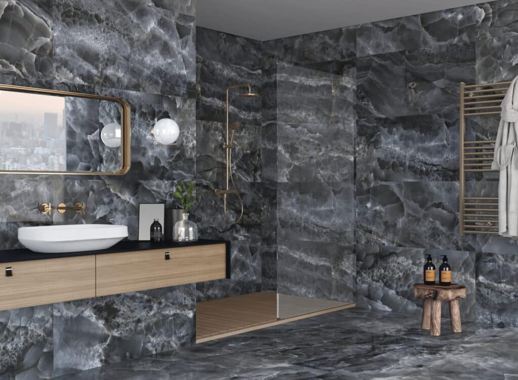 Salle de bain luxueuse avec murs et sol en onyx noir veiné, meuble-lavabo flottant en bois clair, robinetterie or brossé, douche vitrée et tabouret rustique.