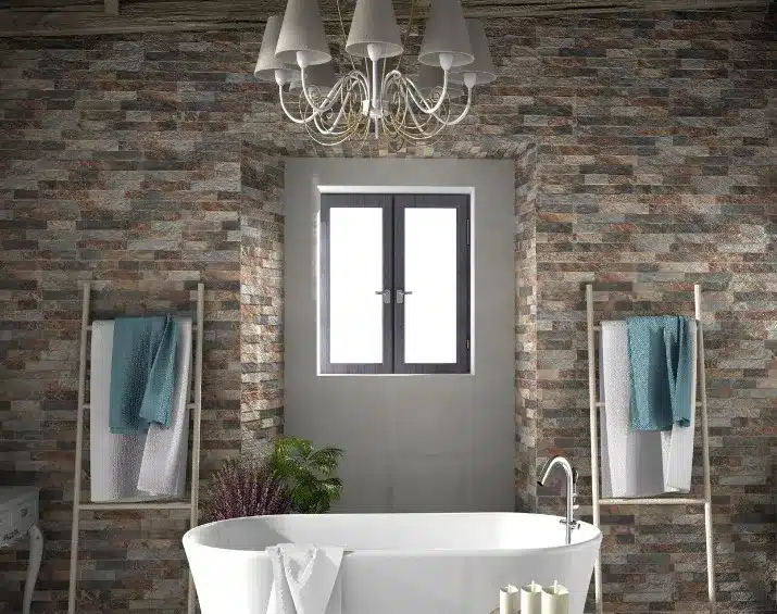 Salle de bain rustique chic avec baignoire îlot blanche, mur en plaquettes de parement pierre naturelle multicolore et lustre moderne.