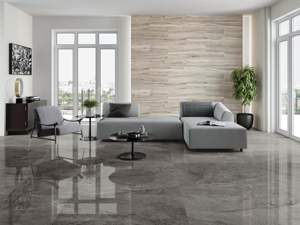 Salon moderne avec canapé gris, fauteuil design et mur d'accent en carrelage aspect bois clair, sol en dalles de pierre polie foncée.