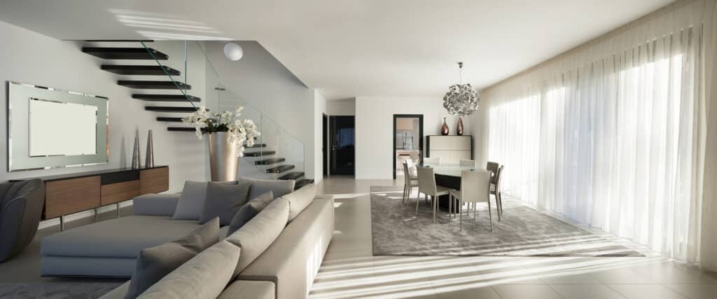 Salon moderne et lumineux avec canapé gris, escalier flottant minimaliste et salle à manger sous un lustre contemporain.