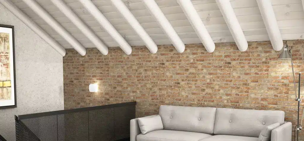 Salon sous combles avec mur en briques apparentes, poutres de toit blanches et canapé clair. Ambiance chaleureuse rustique-moderne.