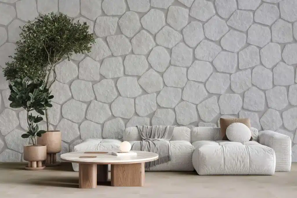 Salon moderne avec canapé blanc texturé et table basse ronde en bois clair devant un mur texturé en fausses pierres blanches de rivière.