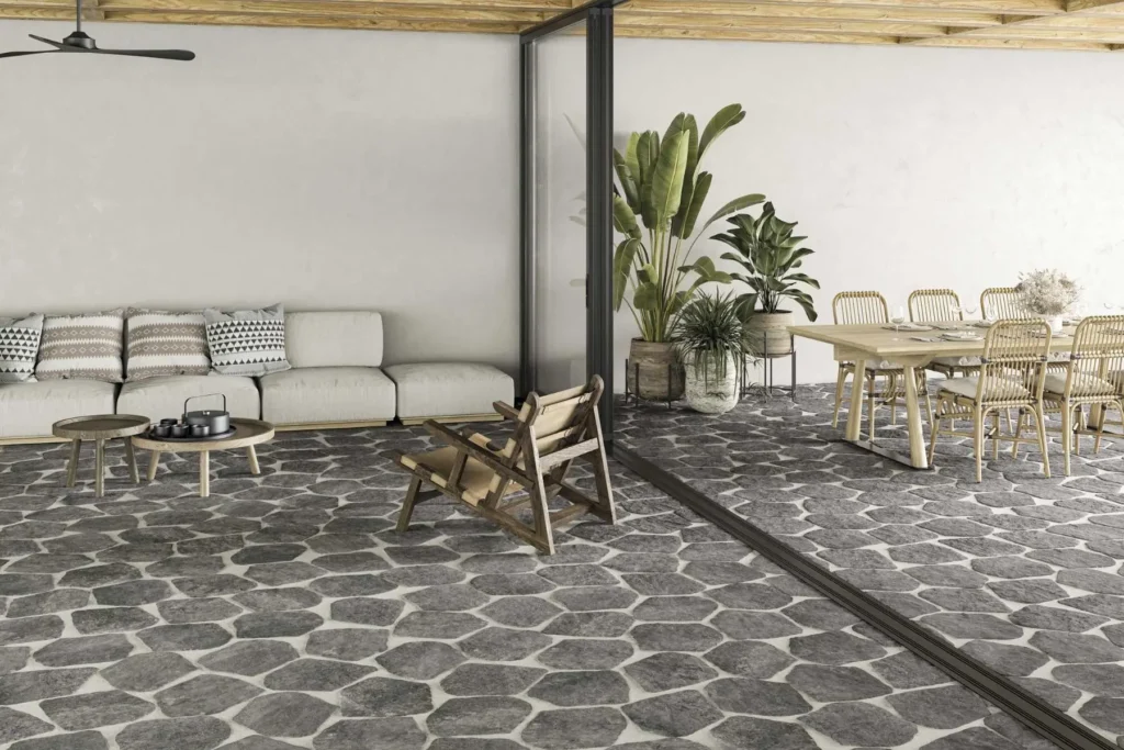 Terrasse extérieure/intérieure moderne avec sol en pavés gris, salon extérieur clair, table à manger en bois et grandes plantes vertes.