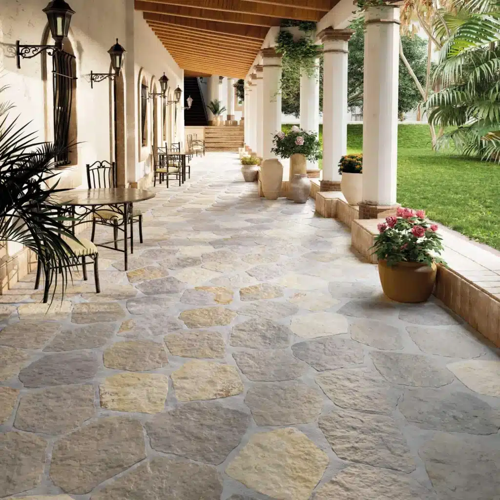 Revêtement de Sol Extérieur en Pierre Naturelle Moderne Terrasse dallée de pierres irrégulières sous une pergola blanche avec colonnes, éclairée par des lanternes murales en fer forgé.