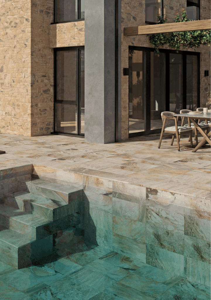 Carrelage en pierre pour piscine et terrasse extérieure Terrasse et margelle en carrelage effet quartzite beige. L'eau turquoise révèle les dalles murales de la piscine. Façade en pierre sèche.