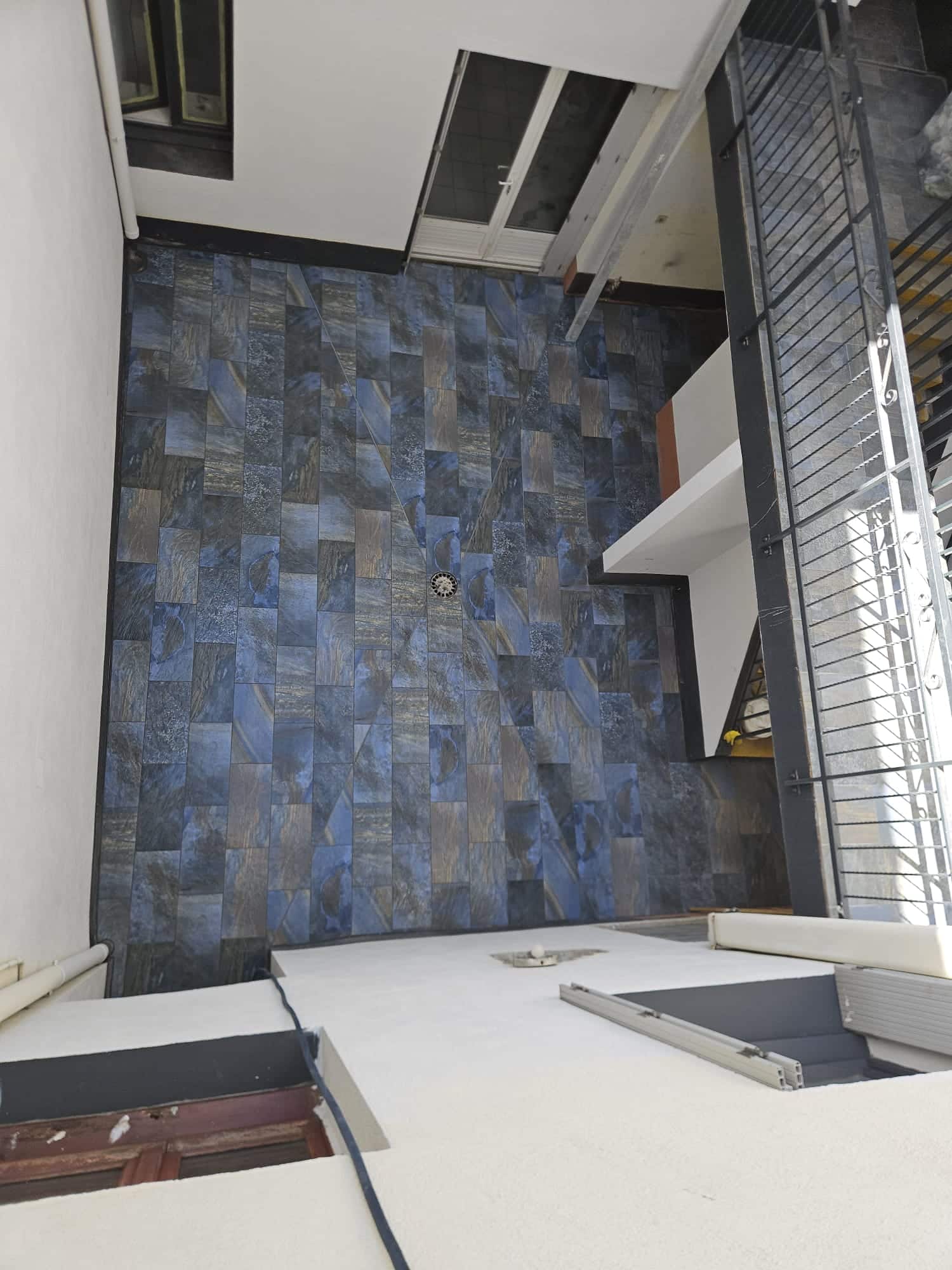 Terrasse moderne carrelée en bleu et brun avec drain central, vue plongeante.