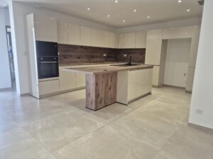 Cuisine moderne avec îlot bois, placards crème brillants et électroménager encastré sur carrelage clair.