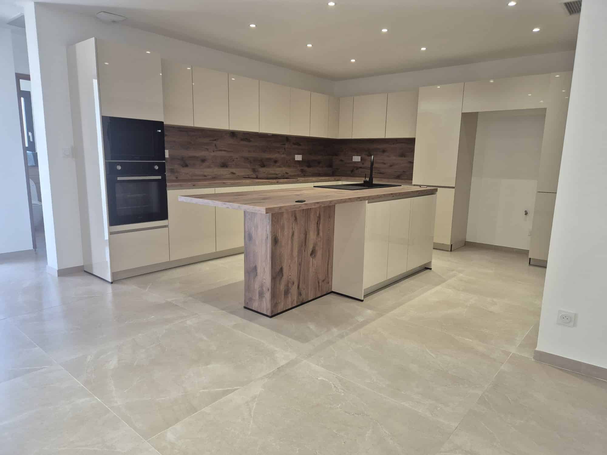 Cuisine moderne avec îlot bois, placards crème brillants et électroménager encastré sur carrelage clair.
