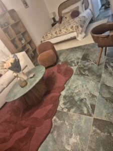Salon avec lit, tapis pétale rouge, table ronde et carrelage marbré bleu élégant.