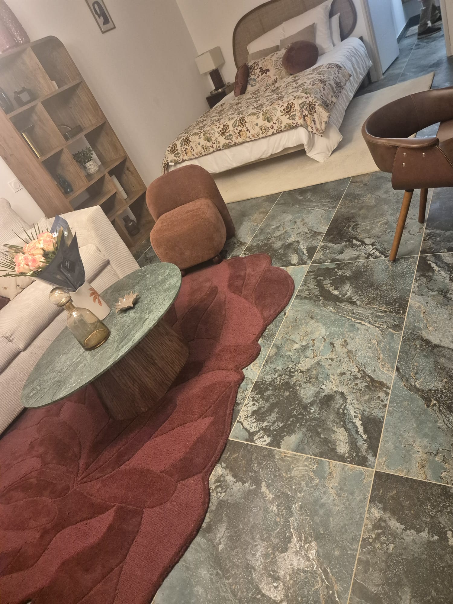 Salon avec lit, tapis pétale rouge, table ronde et carrelage marbré bleu élégant.