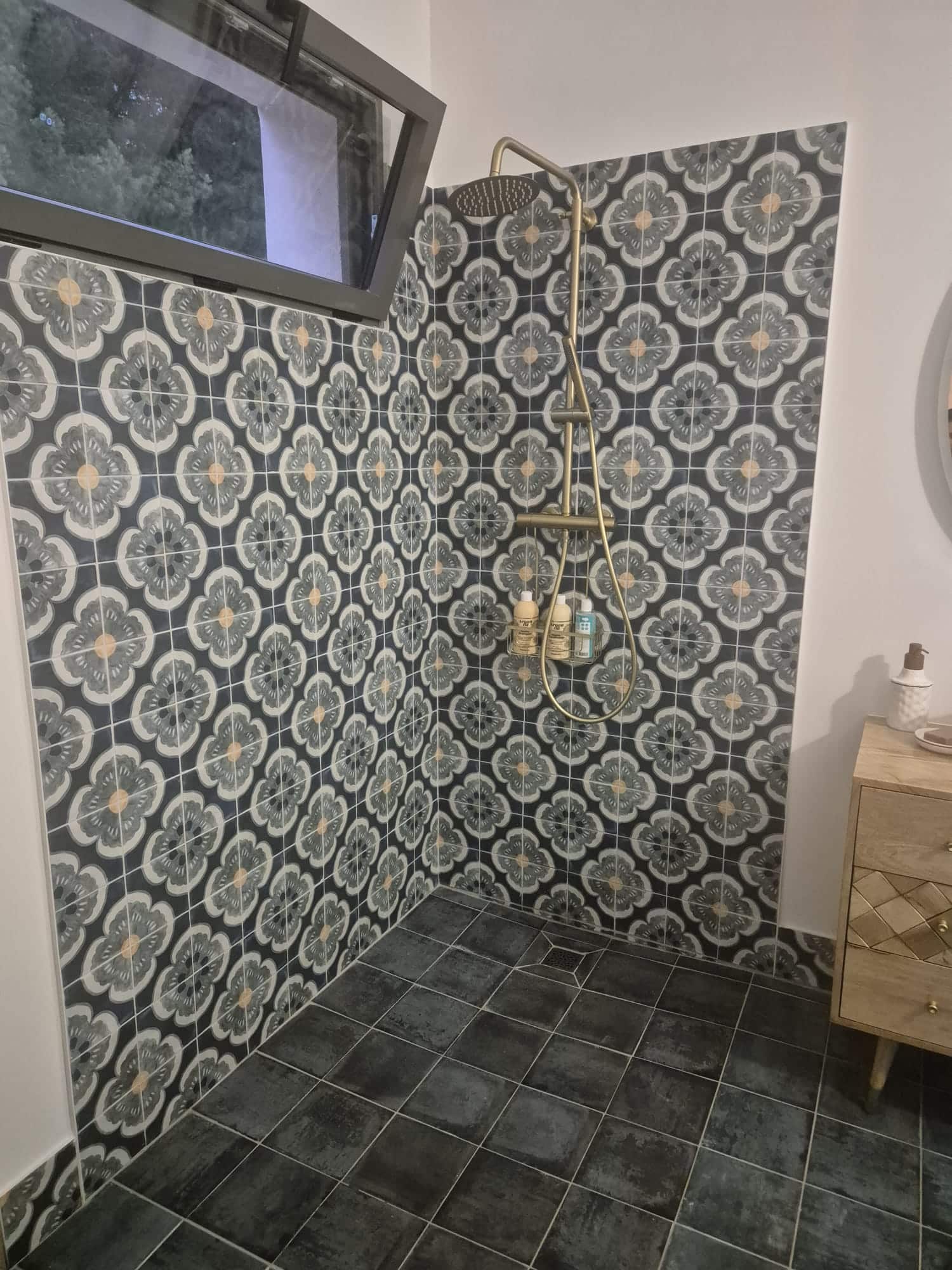 Douche à motifs floraux gris, colonne de douche dorée et carrelage de sol anthracite.