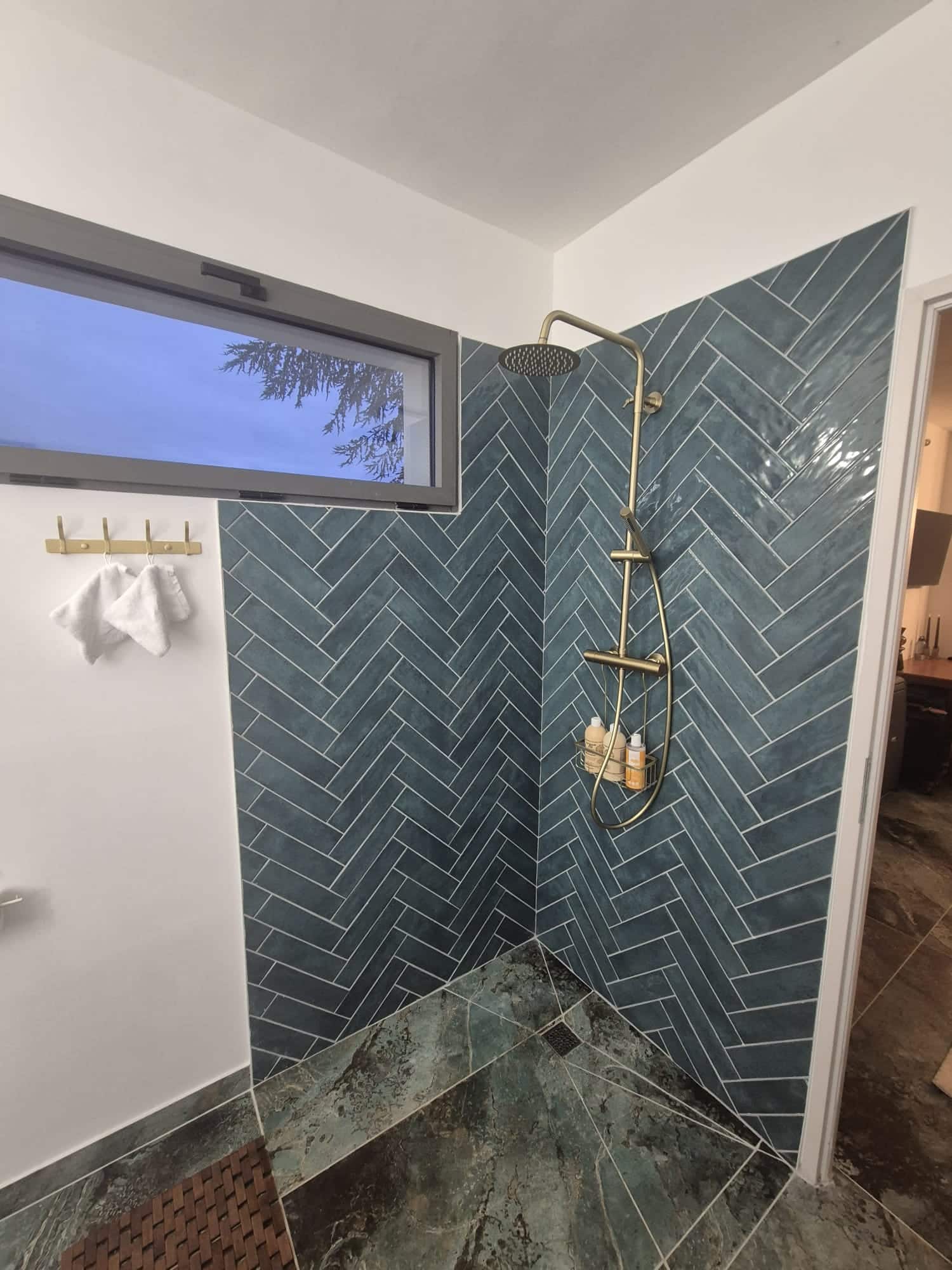 Douche à l'italienne, carrelage bleu en chevrons, sol marbre vert et robinetterie dorée.