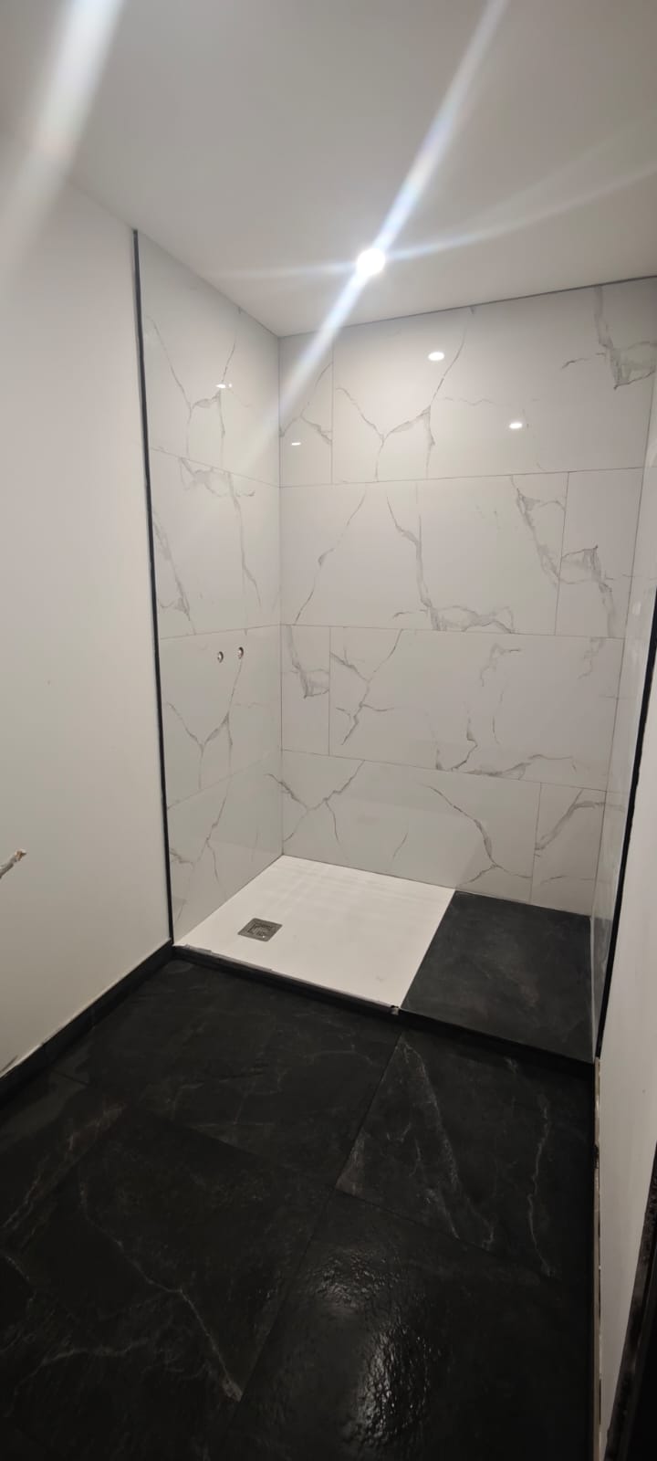 Douche à l'italienne, carrelage mural blanc effet marbre et sol en ardoise noire.