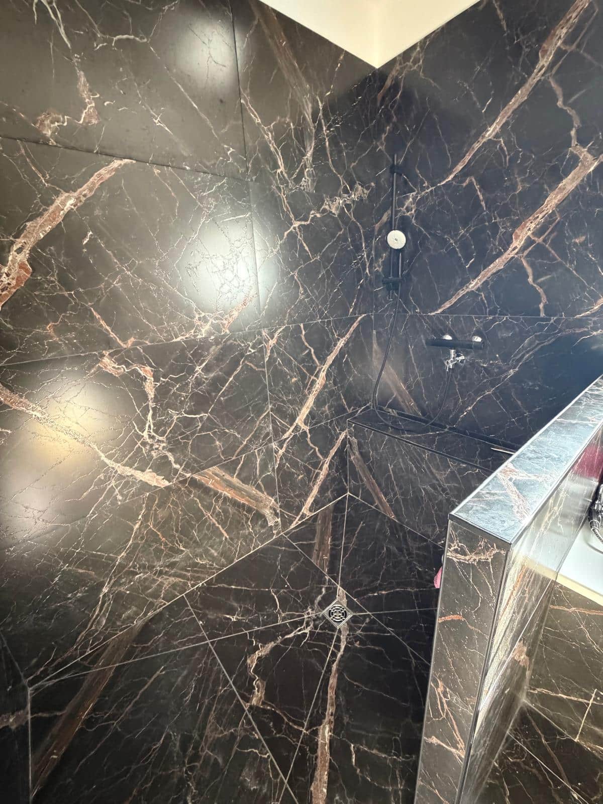 Douche italienne en carrelage effet marbre noir veiné avec robinetterie noire et évacuation centrale.