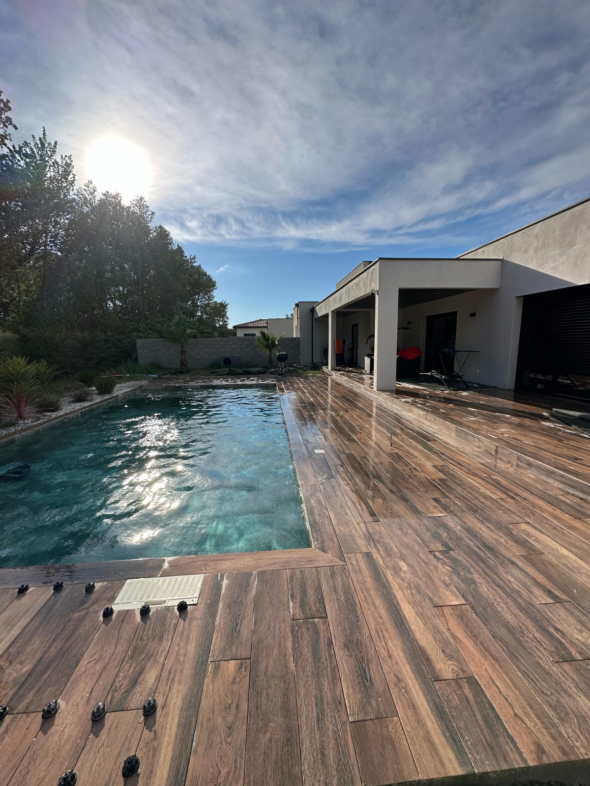 Piscine moderne avec large terrasse aspect bois sous un soleil radieux.