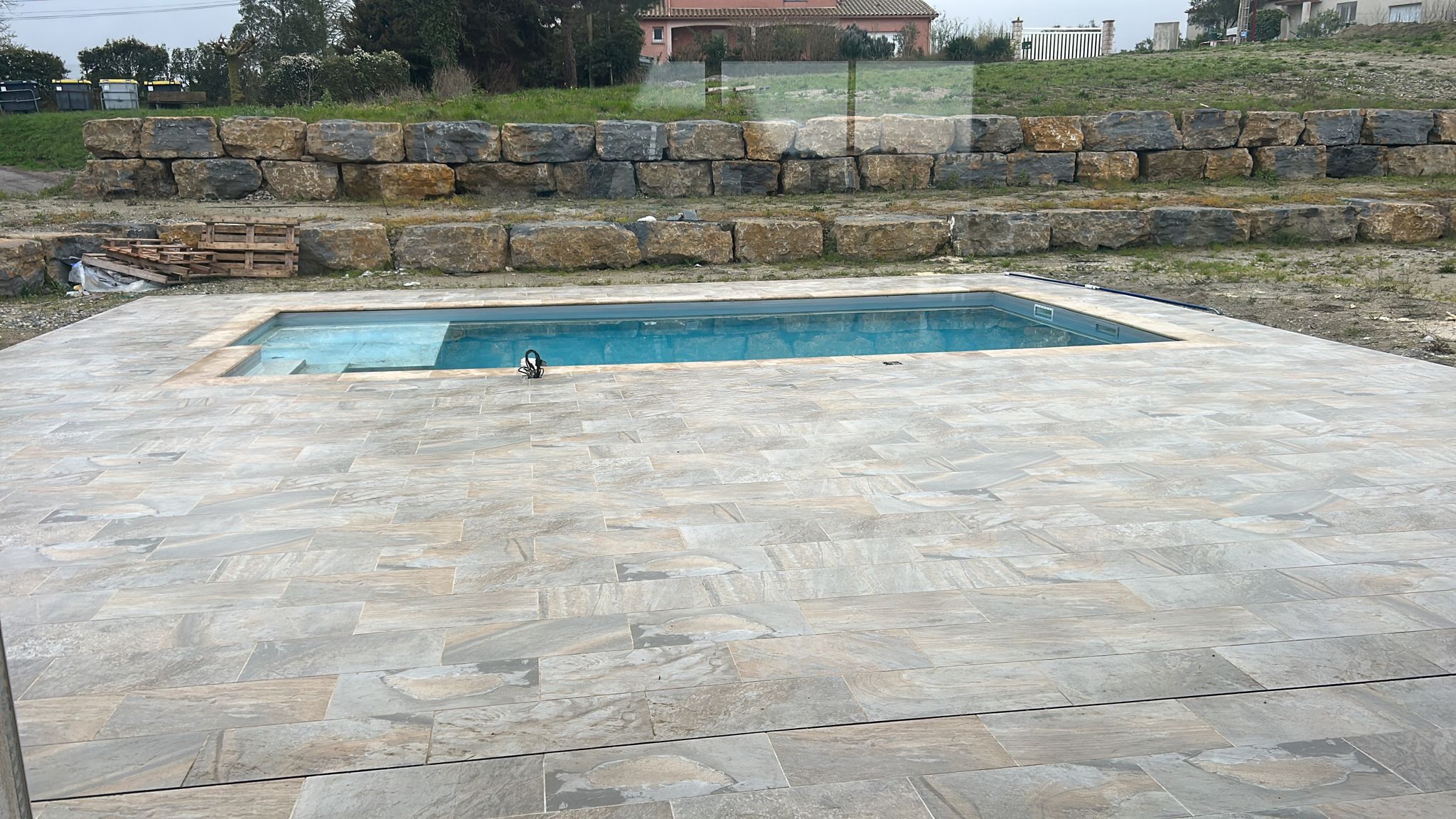 Piscine rectangulaire avec large terrasse dallée et murets de soutènement en pierres naturelles.