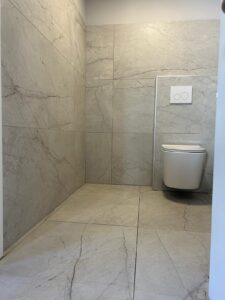 Toilettes suspendues blanches et carrelage gris effet marbre dans une salle de bain moderne.