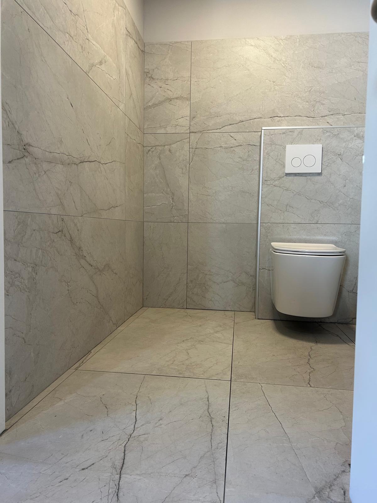 Toilettes suspendues blanches et carrelage gris effet marbre dans une salle de bain moderne.