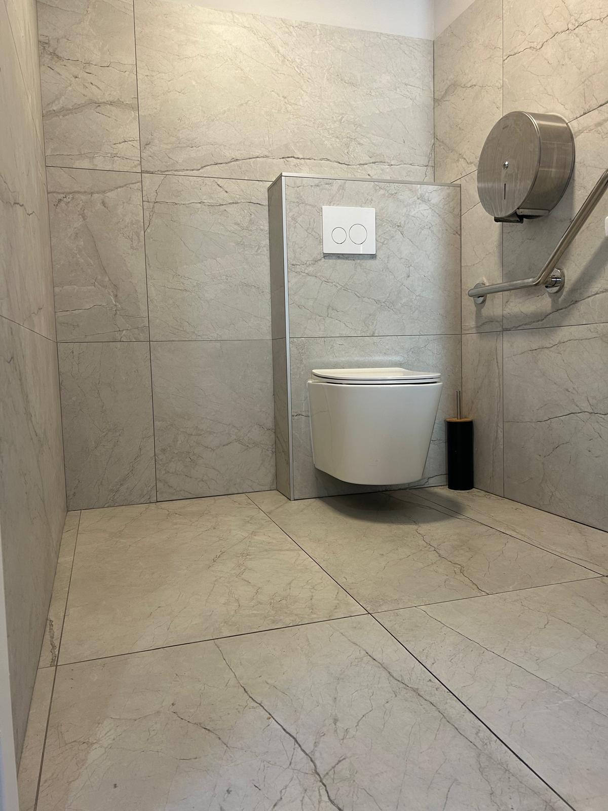 Toilettes suspendues, carrelage marbre gris, barre d'appui et accessoires de salle de bain PMR.